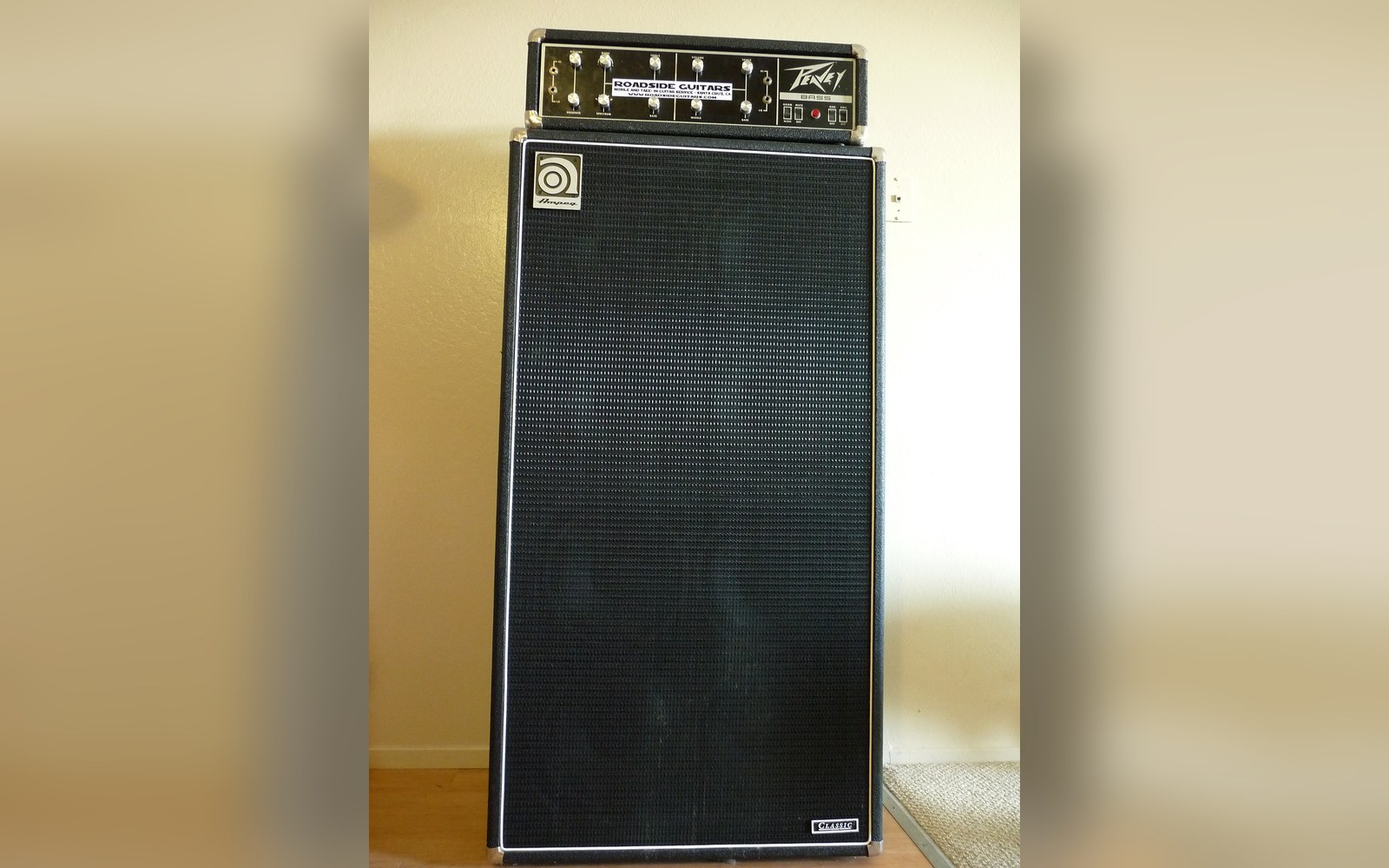 An Ampeg SVT head on an 8×10 cabinet in a rehearsal room, ambient stage lighting, power-amp ventilation slots visible at the top of the head