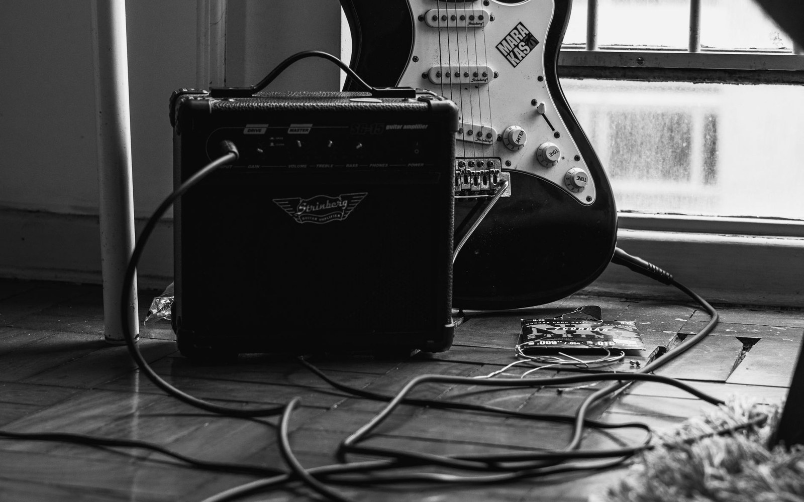 Electric guitar leaning against a small practice amp with cables coiled on the floor