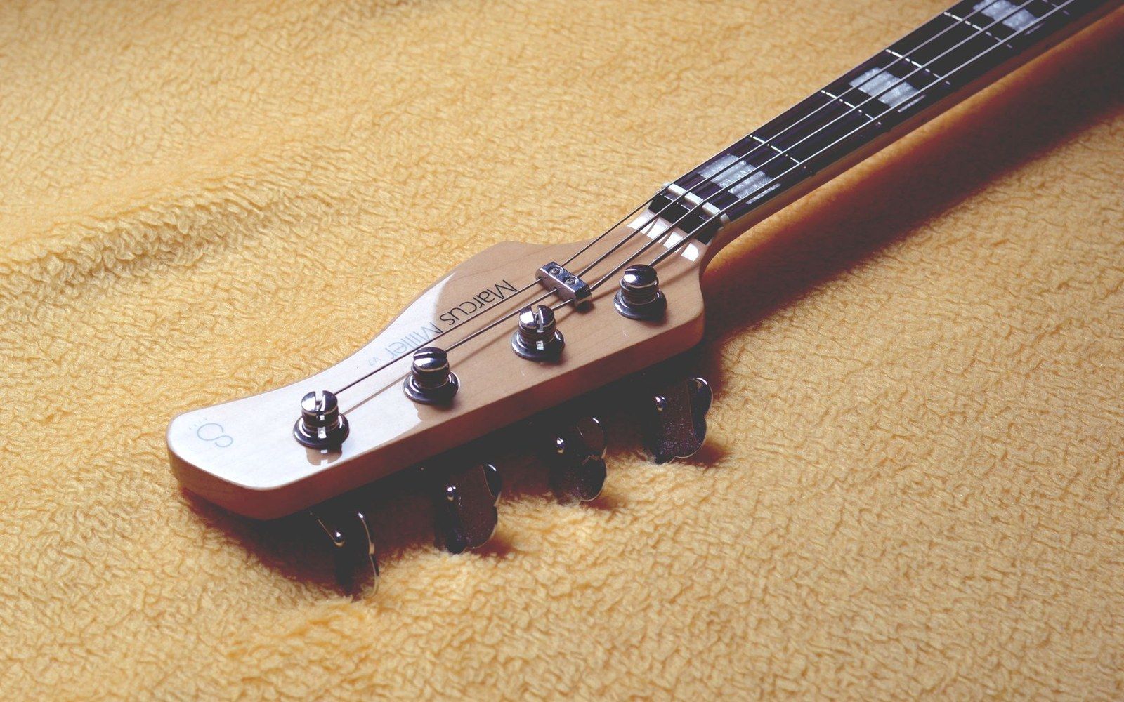 Bass guitar headstock with four tuning pegs resting on a soft yellow blanket