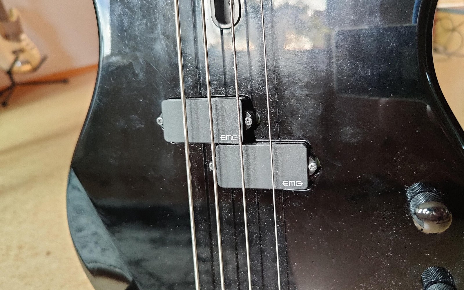 Close-up of a black bass guitar's body showing four strings and two EMG pickups