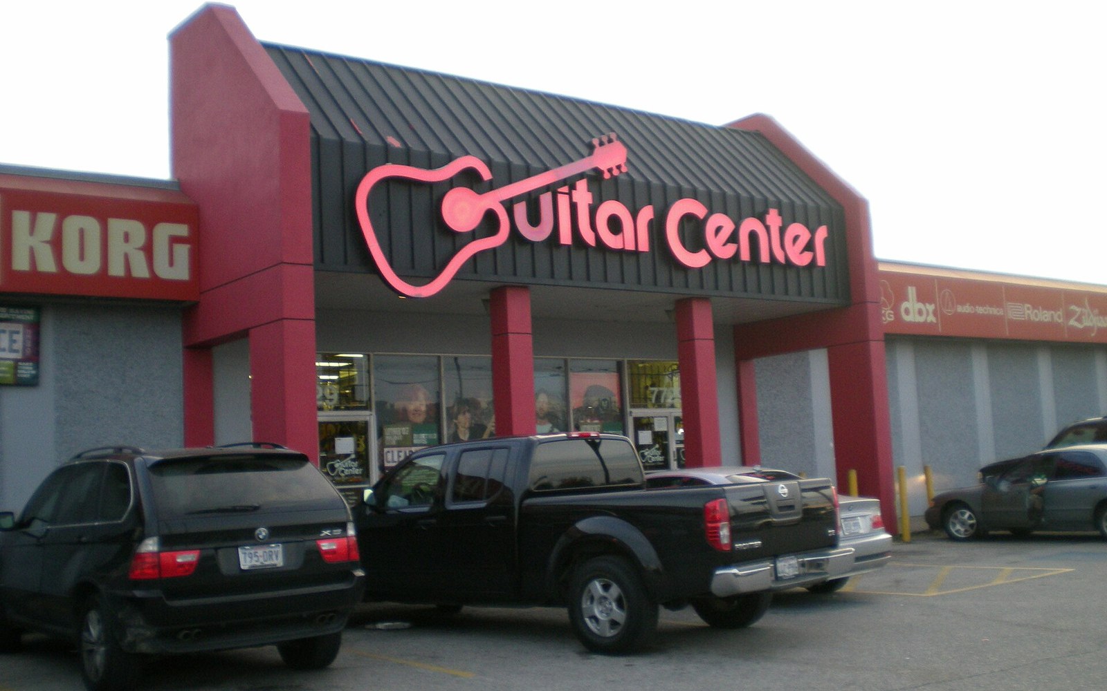 Guitar Center storefront with a guitar-shaped sign, vehicles parked in front