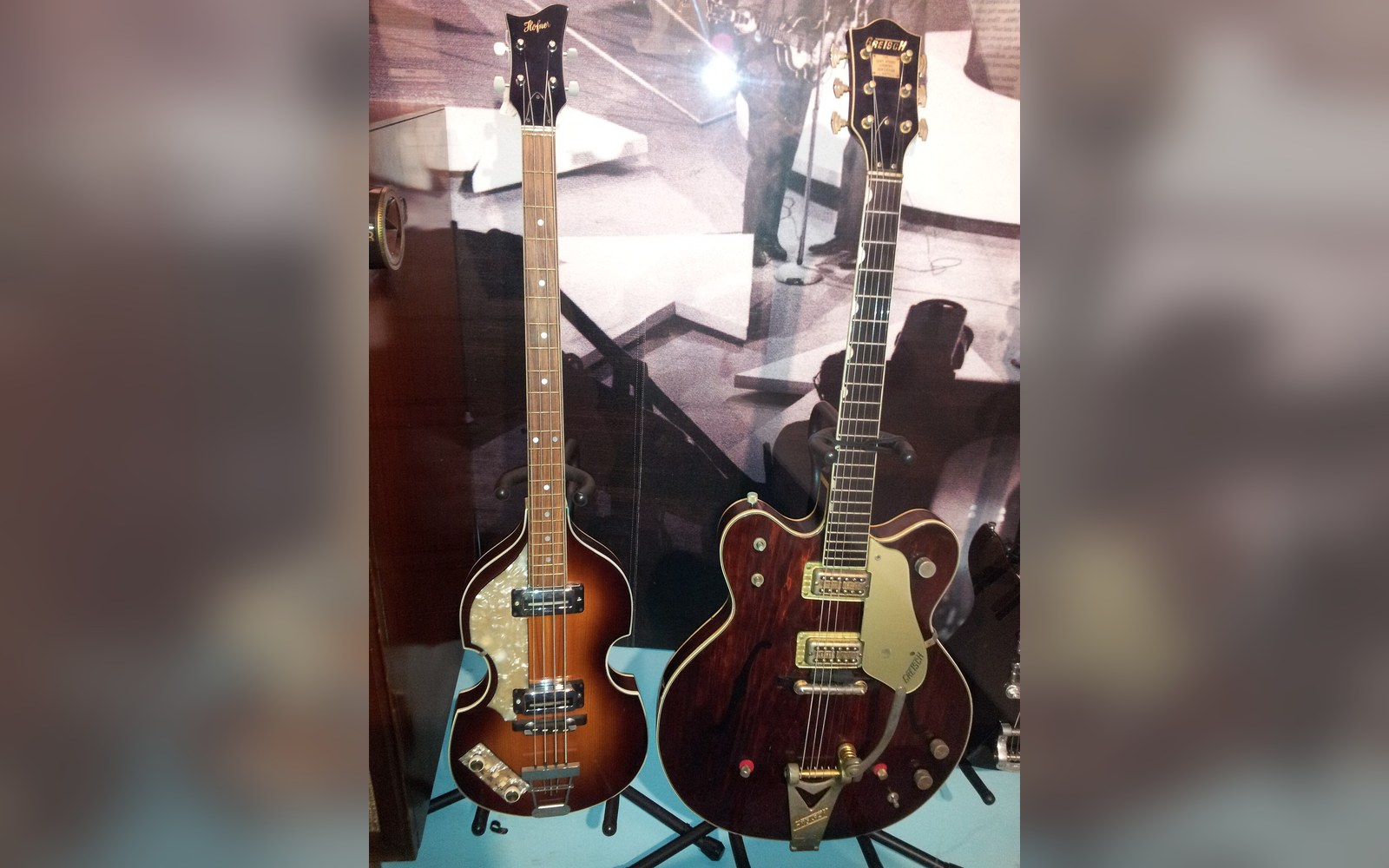 Vintage violin-shaped bass guitar displayed beside a hollow-body electric guitar in a museum case