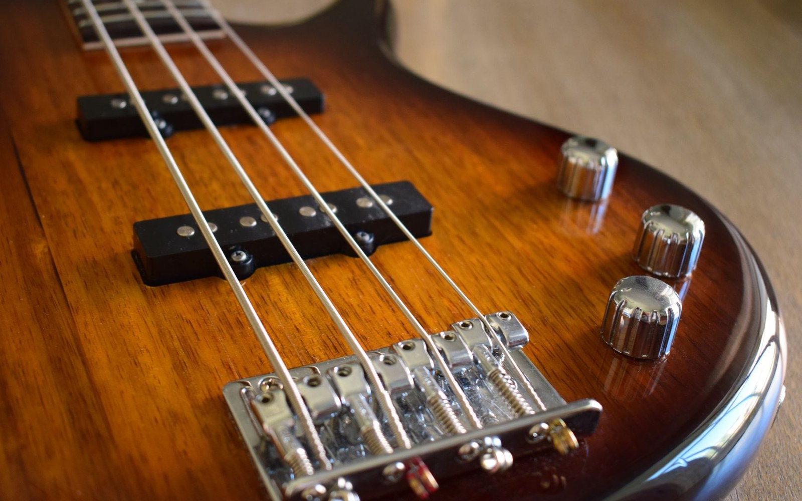 Close-up of a sunburst bass guitar's bridge, pickups and control knobs