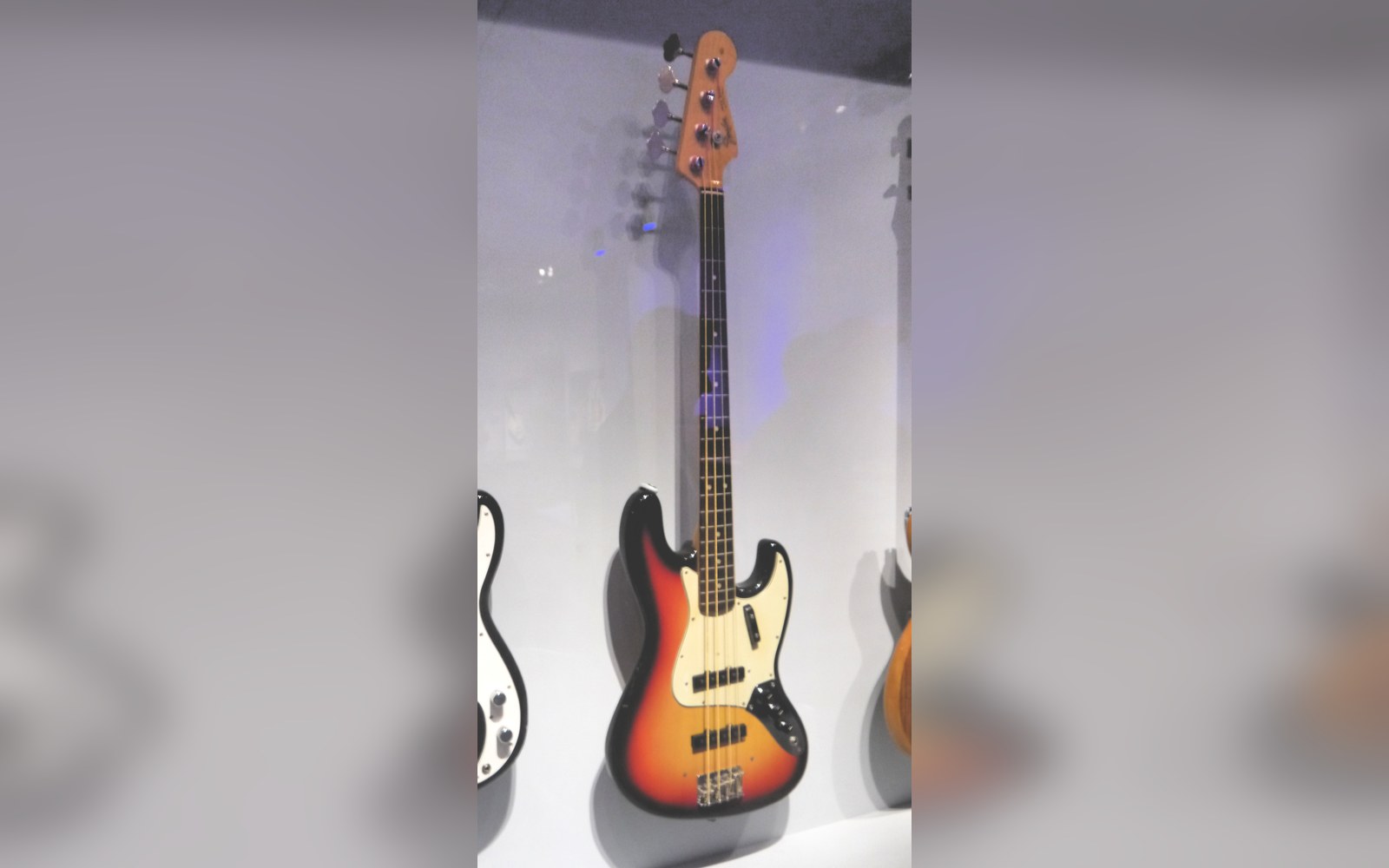 A sunburst Fender Jazz Bass guitar displayed upright in a glass museum case