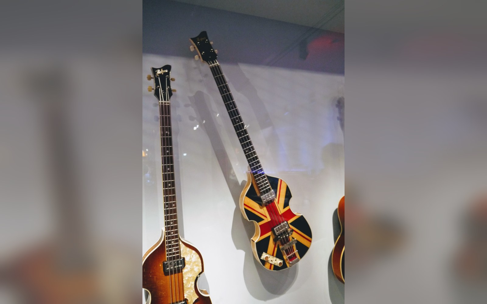 Union Jack-painted violin bass guitar displayed on a wall beside a sunburst bass