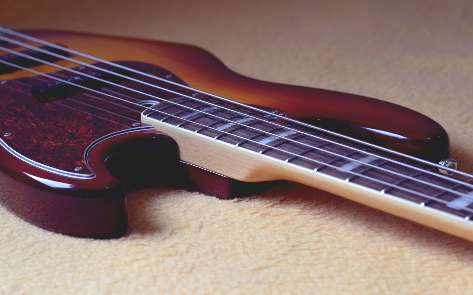 Close-up of a sunburst bass guitar body showing strings, fretboard and tortoiseshell pickguard