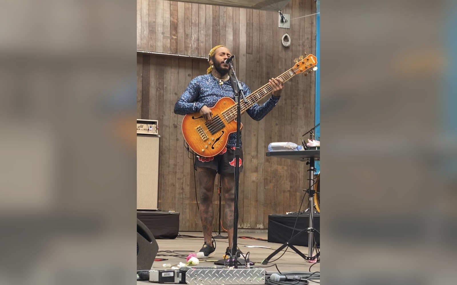 Musician playing a bass guitar into a microphone on an outdoor wooden stage